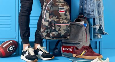Image of person in Polo Ralph Lauren sneakers standing in front of lockers with a football headphones, Levi's® backpacks, Polo Ralph Lauren sneakers and jean jacket