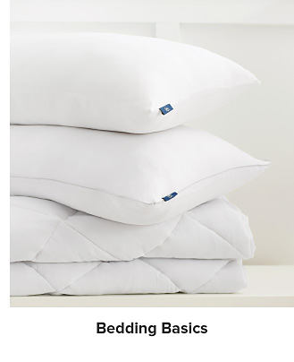 A stack of white pillows and mattress toppers. Shop bedding basics.