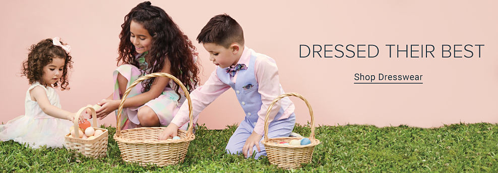 Three children putting eggs in their Easter baskets. Dressed their best. Shop Dresswear.