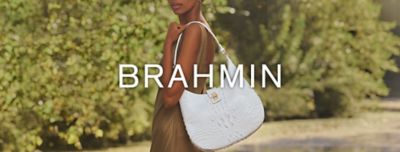 A woman stands outside with a white Brahmin handbag on her should. Shop Brahmin.