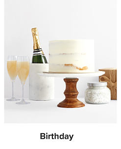 An image of a white birthday cake on a stand with a bottle of champagne beside it. Shop birthday. 