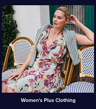 A woman in a floral dress with a gray sweater draped across her shoulders. Shop women's plus clothing.