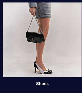 A woman in a gray business dress and heels holding a black handbag. Shop shoes.