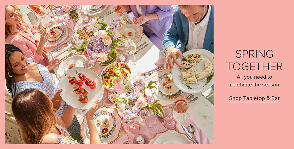 An image of a group of men and women in dresswear, seated at an outdoor table filled with food and decorated with spring colors. Spring together. All you need to celebrate the season. Shop tabletop and bar. 