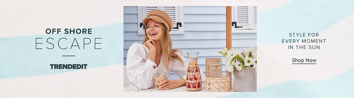 An image of a woman wearing a white blouse and a tan hat sipping a drink at a table with drinkware and a vase with flowers on a table. Off shore escape. Trend Edit. Style for every moment in the sun. Shop Now.