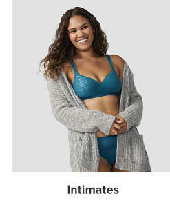 A woman in a matching blue bra and panty set and a gray cardigan. Intimates.