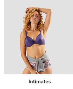 A woman in a purple bra and floral panties with a crewneck tied around her waist. Intimates.