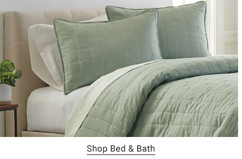 A bed made up with white sheets and a light green comforter and pillows. Shop Bed and Bath. 