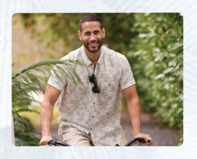 An image of a man on a bike wearing a floral short sleeve button front shirt. Stay cool all spring.