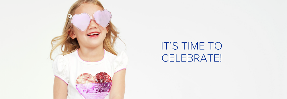 A little girl wearing heart shaped sunglasses and a white tee shirt with a heart shaped sequin applique. It's time to celebrate!