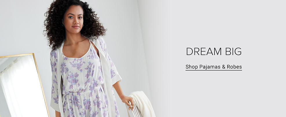An image of a woman wearing a white and purple floral print pajama set with a matching robe. Dream big. Shop pajamas and robes.