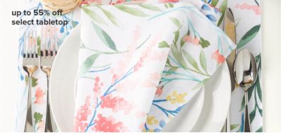 A floral tablecloth, on top of which sits a white plate with cutlery and a napkin with the same floral pattern on top of the plate. 55% off select tabletop.