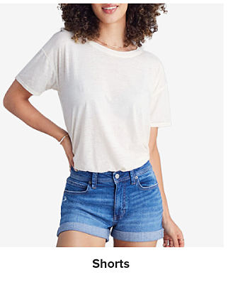An image of a young woman wearing a white tee and denim shorts. Shop shorts.