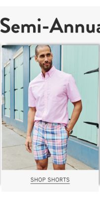 A man wearing a pink short sleeved button front shirt & blue & white plaid shorts. Shop shorts.