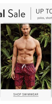 A man wearing red & black patterned print swim trunks. Shop swimwear.