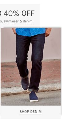 A man wearing a blue short sleeved button front shirt with white dots, blue jeans & navy sneakers. Shop denim.