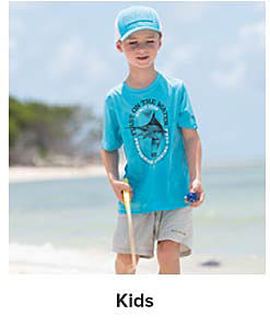 A boy in khaki shorts, and a teal shirt and hat. Shop kids.