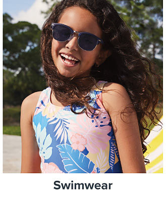 An image of a girl wearing a swimsuit and sunglasses. Shop swimwear. 