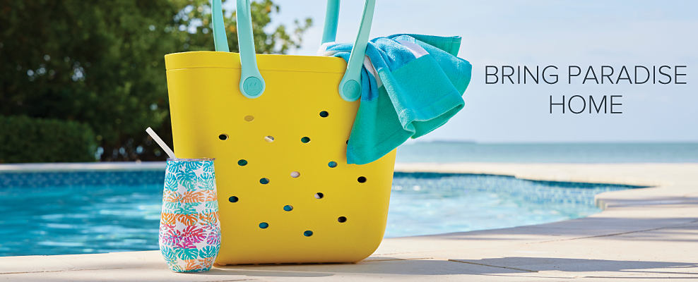 An image featuring a beach bag, beach towel and cup sitting next to a swimming pool. Bring paradise home.