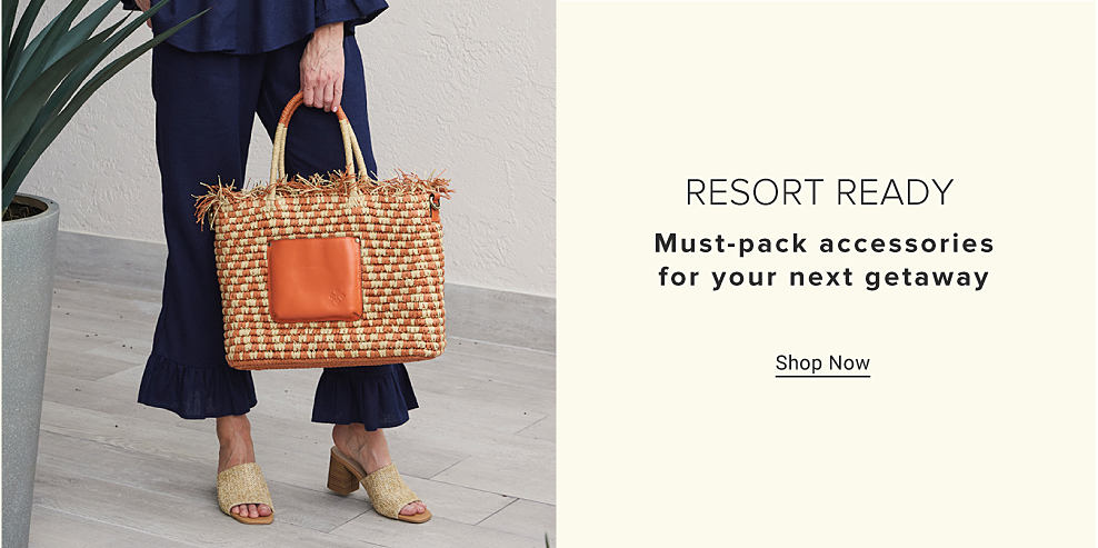 An image of a woman wearing a navy outfit, holding a woven handbag. Resort ready. Must pack accessories for your next getaway. Shop now.