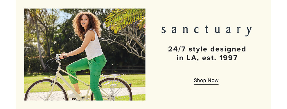 A woman riding a bike wearing a white tank and green pants. Sanctuary. 24 7 style designed in LA, est. 1997. Shop now.