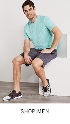 A man wearing a light green T shirt, gray shorts & navy sneakers. Shop men.