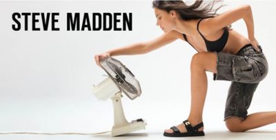 Steve Madden. Image of a woman in a black bra, black shorts and black sandals in front of a fan.