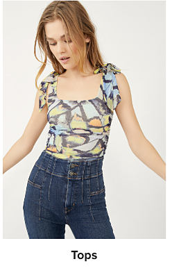 A woman wearing a colorful abstract print sleeveless blouse and high waisted jeans. Shop tops.