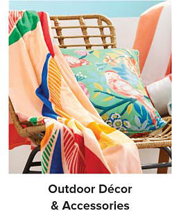 An image of a bright pillow and beach towel on a brown wicker chair. Shop outdoor decor and accessories. 