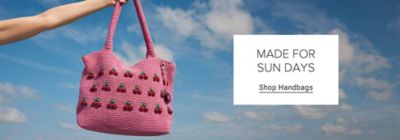 A pink handbag with cherries on it against a cloud filled sky. Made for sun days. Shop handbags.