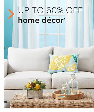 A gray couched with a light blue pillow with a yellow lemon on it. On the table in front of it sets a small lemon plant decoration, and bottles on a wooden tray. Up to 60% off home decor.