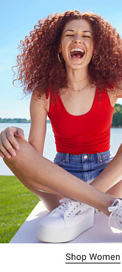 Young woman wearing a red tank top, denim shorts and white sneakers. 