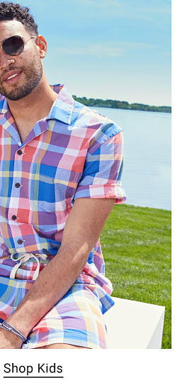 Man wearing a plaid red, white and blue button down shirt and matching shorts.