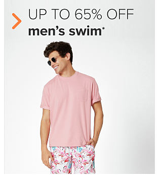 A man in a pink tee with pink, white and teal swim trunks. Up to 60% off men's swim. 