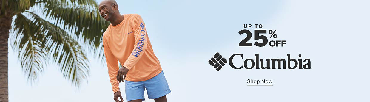 An image of a man in an orange Columbia long sleeve shirt and blue Columbia shorts, with a palm tree behind him. Up to 25% off Columbia. Shop now.