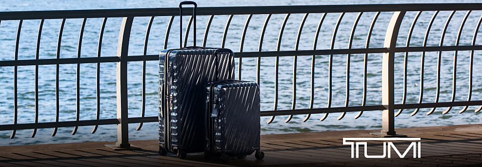 An image of two spinner suitcases sitting in front of a body of water. Tumi.