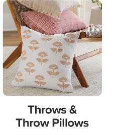 Square pillow with flowers leaning against a chair. Shop throws and throw pillows.