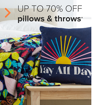 A blue throw blanket with bright flowers, and a blue pillow with a sun pattern that says yay all day. Up to 70% off pillows and throws. 
