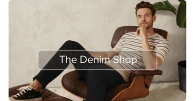 A man in a striped shirt and dark jeans sitting in a brown chair. The Denim Shop.