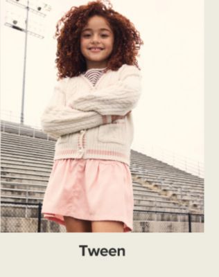 A girl in a cardigan and pink skirt. Shop tween.