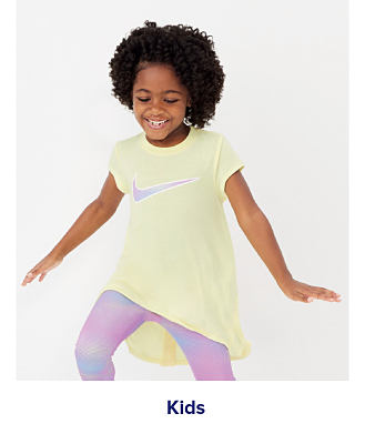 A girl in a yellow Nike shirt and tie dye leggings. Shop kids. 
