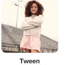 A girl in a white sweater and pink skirt. Shop tween.