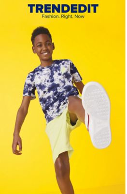 A boy in a blue and white tie dye shirt and yellow shorts holds his foot up as if in the middle of a step. Trend Edit. Fashion right now. 