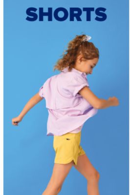  A girl wears a purple button up shirt with rolled up cuffs and yellow shorts. Shorts. 