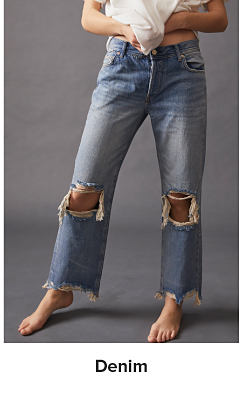 A woman in a white top and blue jeans that are ripped at the knee. Denim. 