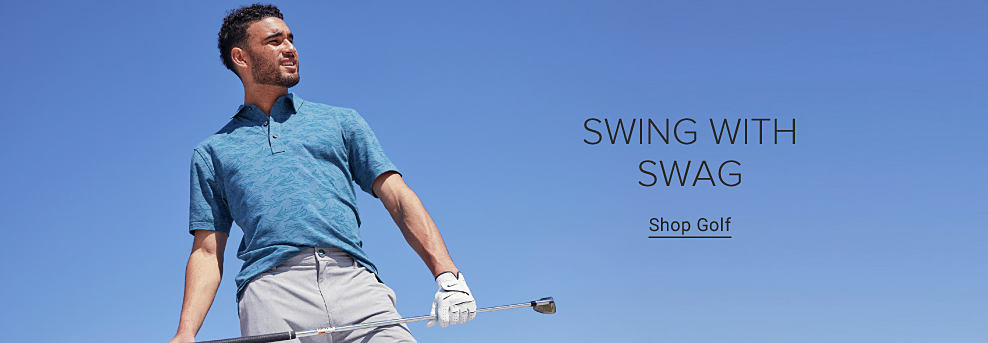 A man holding a golf club wearing a blue short sleeve polo shirt and khakis and a golf glove. Swing with swag. Shop golf.