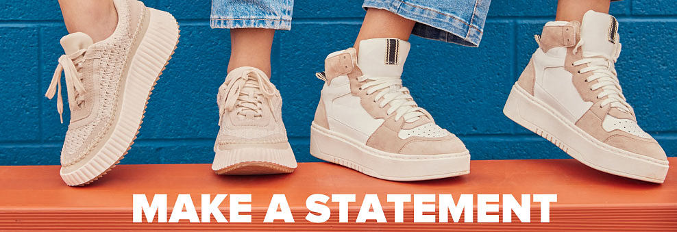 Two people wear beige and white sneakers in front of a blue wall. Make a statement. 