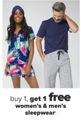 A woman in a mathing short sleeve pajama set in navy with hot pink and green tropical designs and a navy eye mask. A man in a navy tee shirt and gray checkered pajama pants. Buy 1, get 1 free women's and men's sleepwear. 