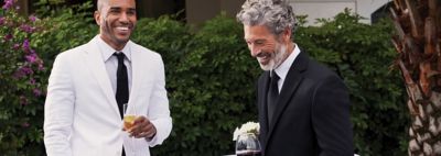 An image of a man in a white suit with a black tie standing next to a man wearing a black suit and tie.