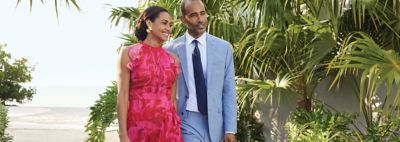 An image of a man wearing a blue suit walking with a woman wearing a sleeveless ruffled dress.